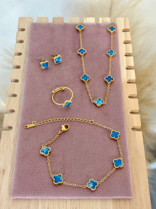 4-piece gold stainless steel jewelry set featuring mini baby blue enamel four-leaf clover 5-motif necklace (16-18 inch), bracelet, stud earrings, and adjustable ring on a purple display.⁠