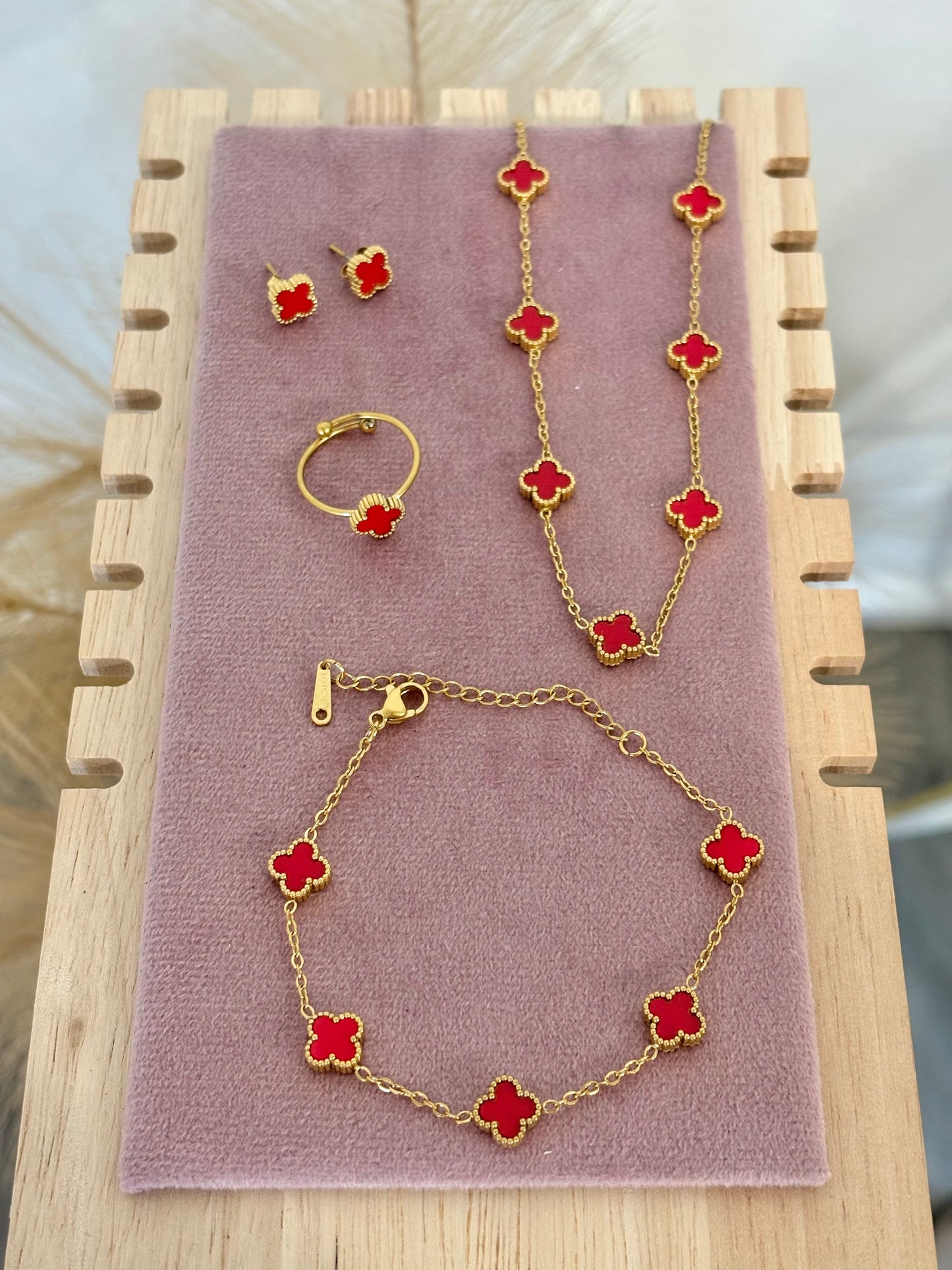 4-piece gold stainless steel jewelry set featuring mini red enamel four-leaf clover 7-motif necklace, 5-motif bracelet, stud earrings, and adjustable ring on a mauve velvet display.⁠