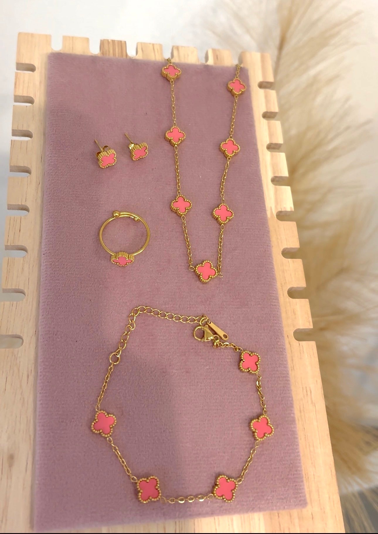 4-piece gold stainless steel jewelry set featuring mini light pink enamel four-leaf clover 5-motif necklace, 5-motif bracelet, stud earrings, and adjustable ring on a purple velvet display.⁠