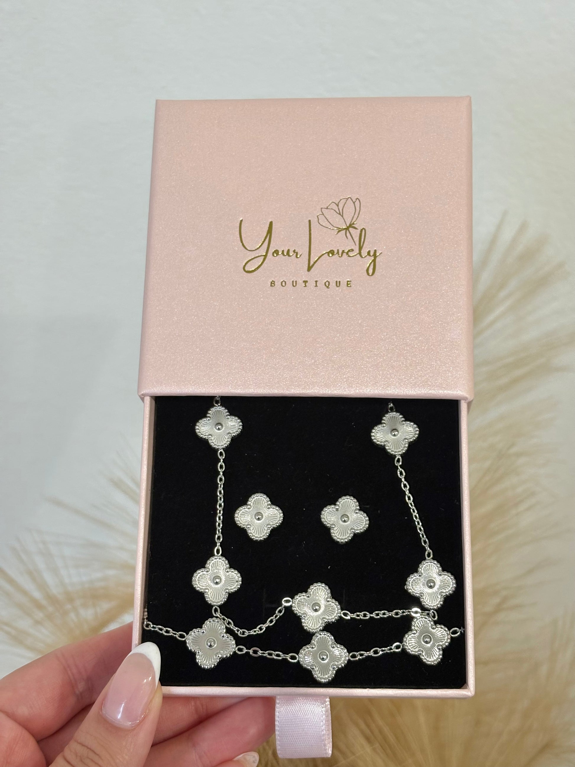 3-piece silver stainless steel jewelry set featuring textured guilloche four-leaf clover 5-motif necklace, stud earrings, and matching bracelet on a mauve display.⁠
