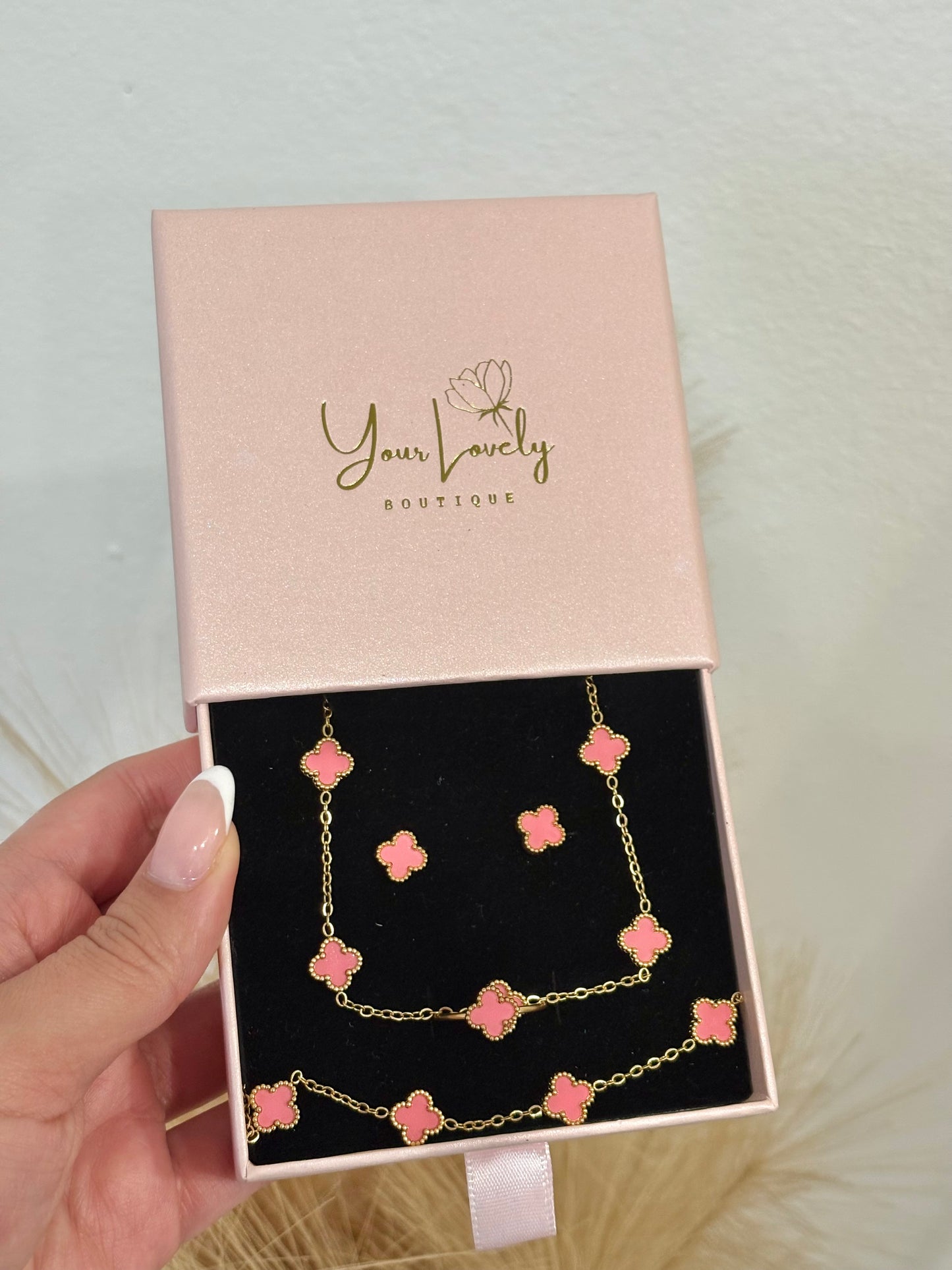 4-piece gold stainless steel jewelry set featuring mini light pink enamel four-leaf clover 5-motif necklace, 5-motif bracelet, stud earrings, and adjustable ring on a purple velvet display.⁠