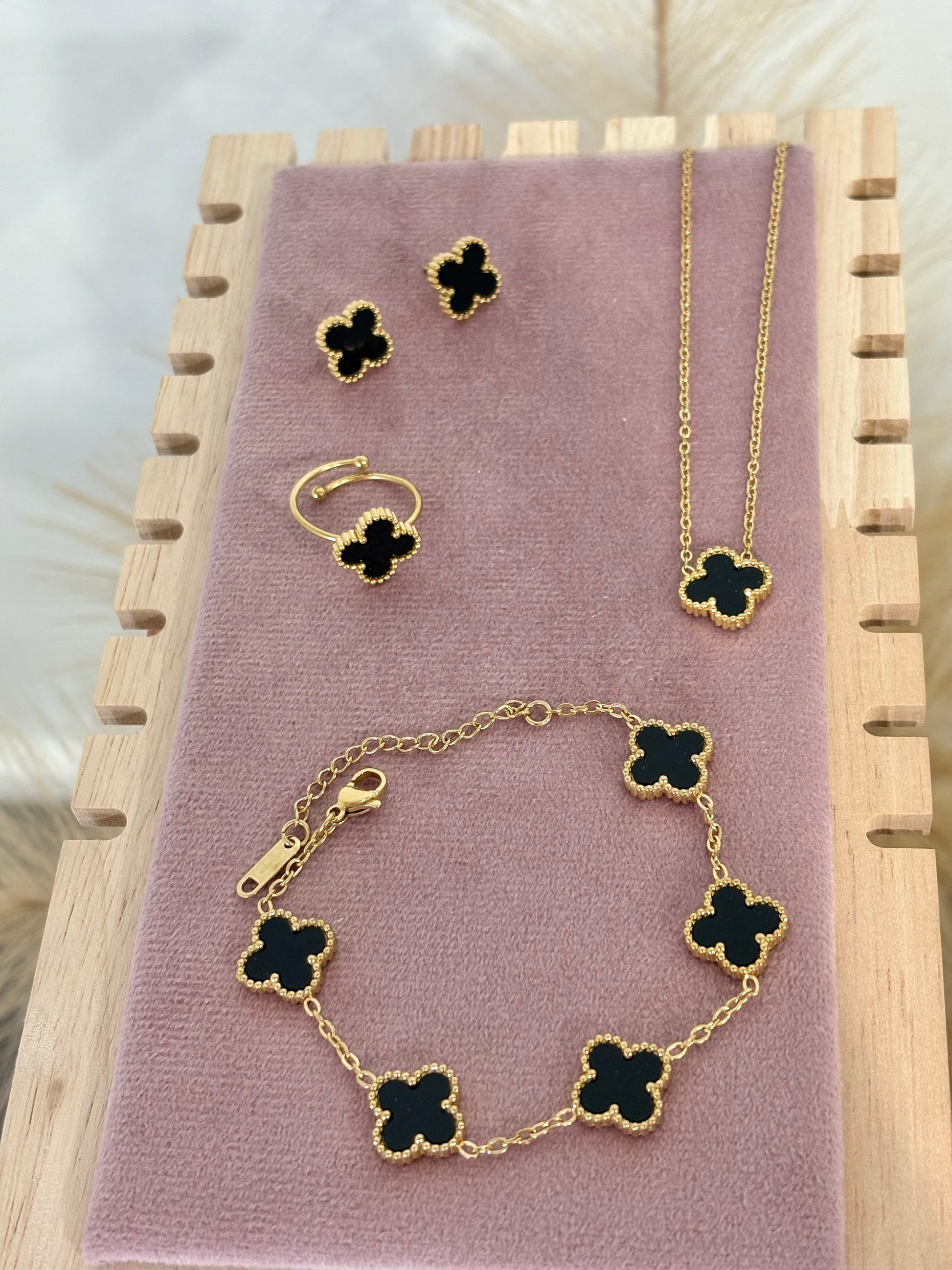 4-piece gold stainless steel jewelry set featuring mini black enamel four-leaf clover necklace, stud earrings, five-motif link bracelet, and adjustable ring on a purple display.⁠