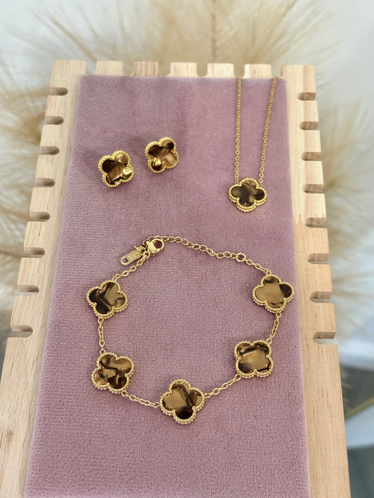 3-piece gold stainless steel jewelry set featuring brown enamel four-leaf clover necklace, stud earrings, and multi-clover bracelet displayed on a purple velvet stand.⁠